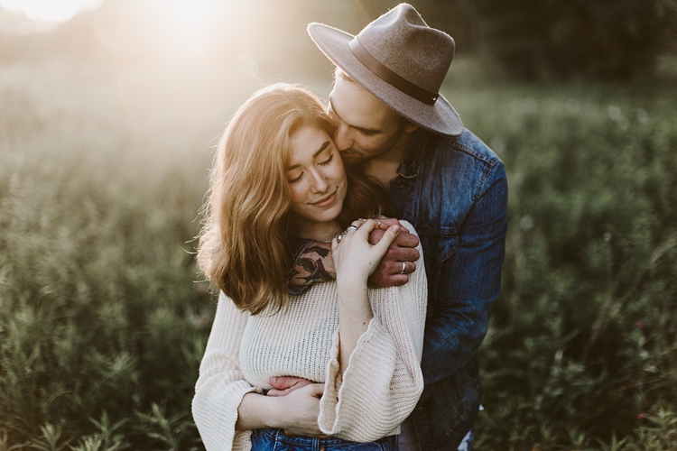 Hipster couple kissing in the field with the sun behind them
