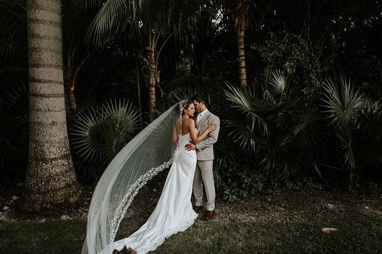 Bride and groom kissing by palm trees at Grand Palladium Mexico